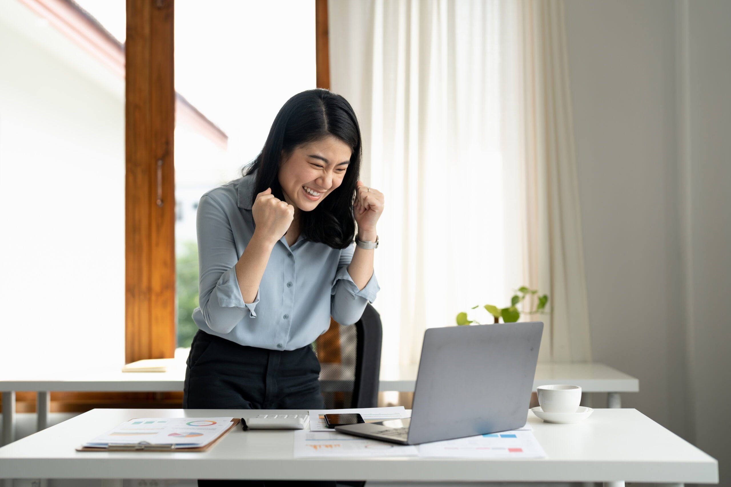 excited young woman standing at table with laptop 2022 10 07 21 20 13 utc scaled